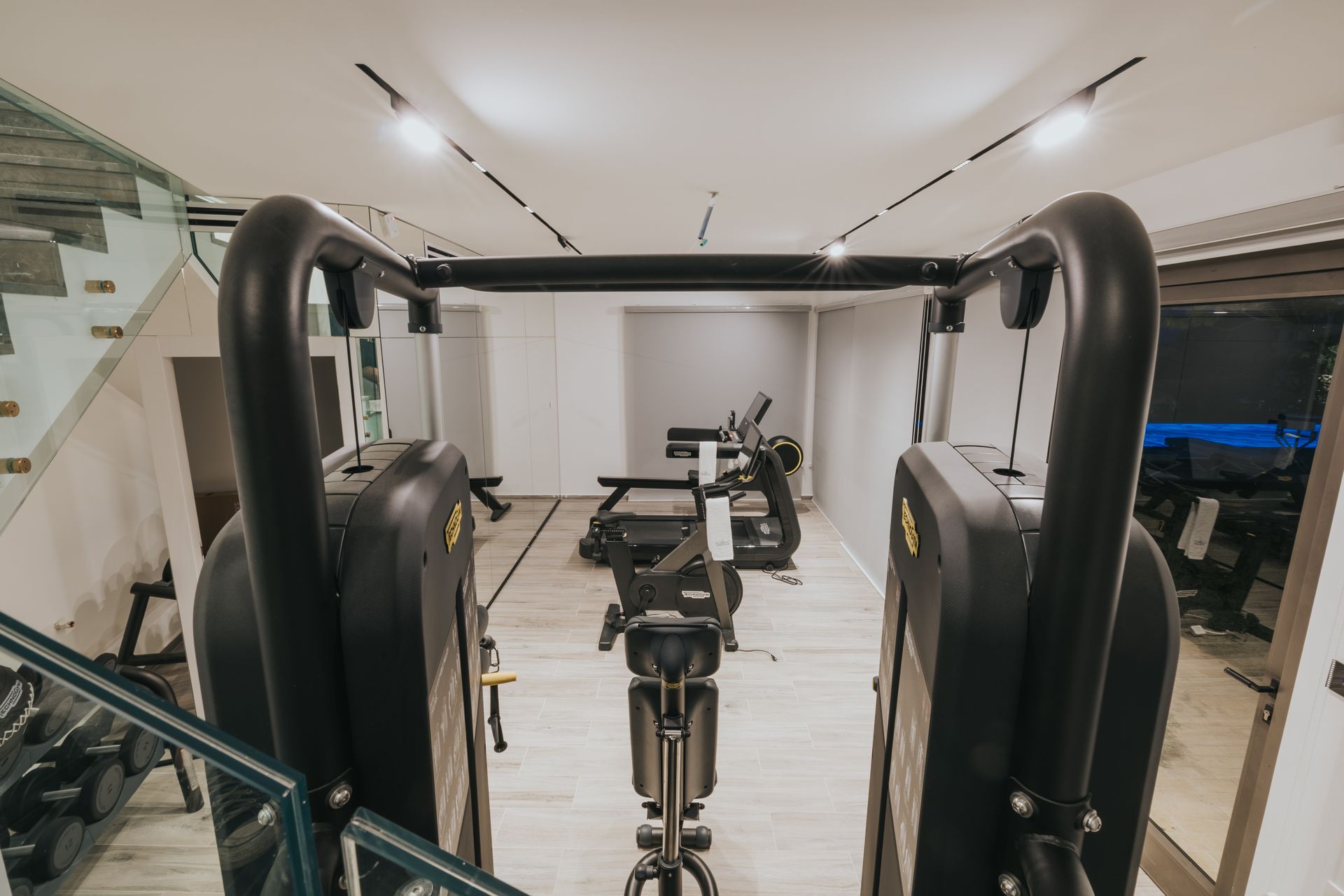 Gym interior with exercise equipment: treadmills, bikes, and free weights, stairs on the left.