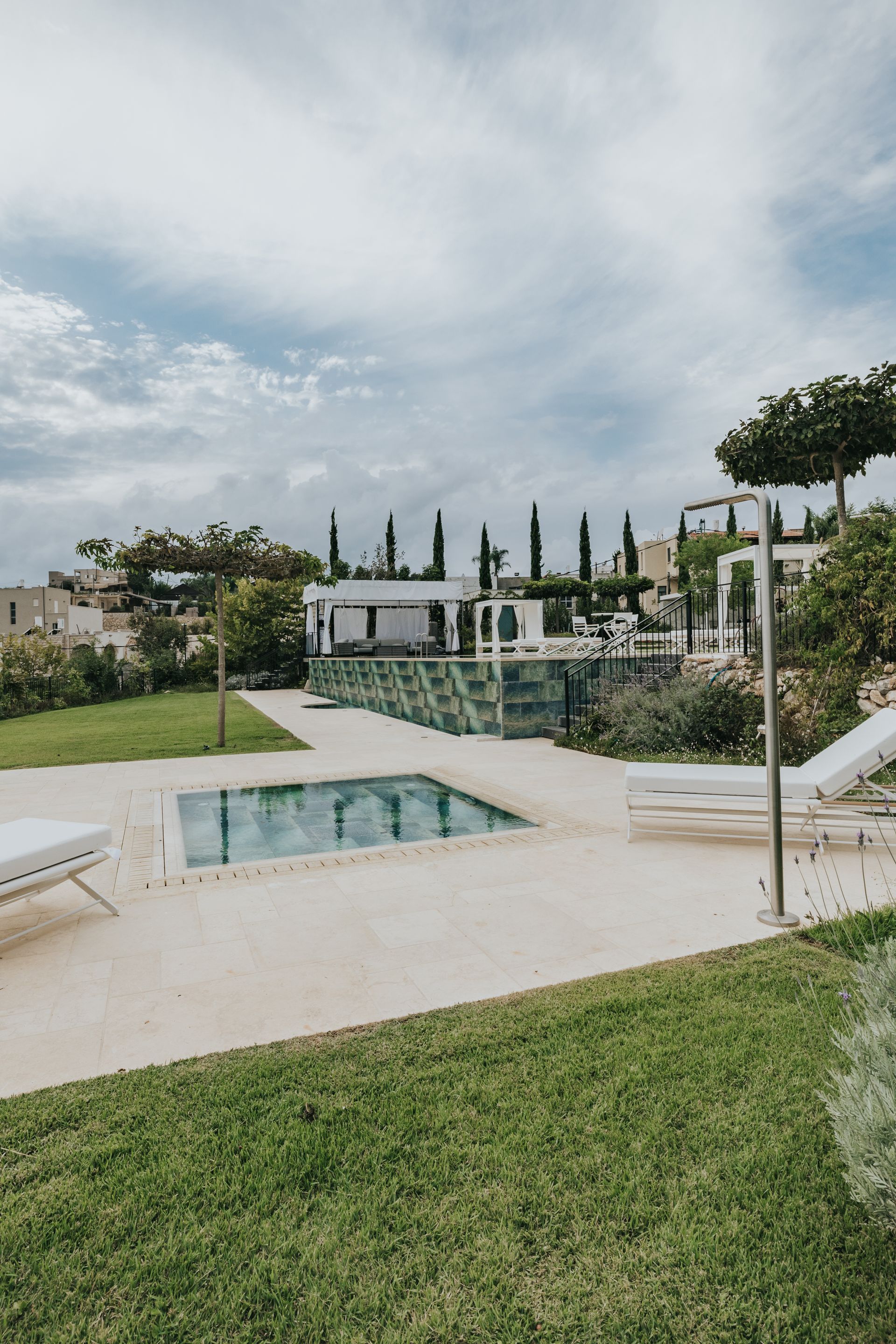 Poolside scene: small pool, white lounge chairs, green lawn, trees, and cloudy sky.