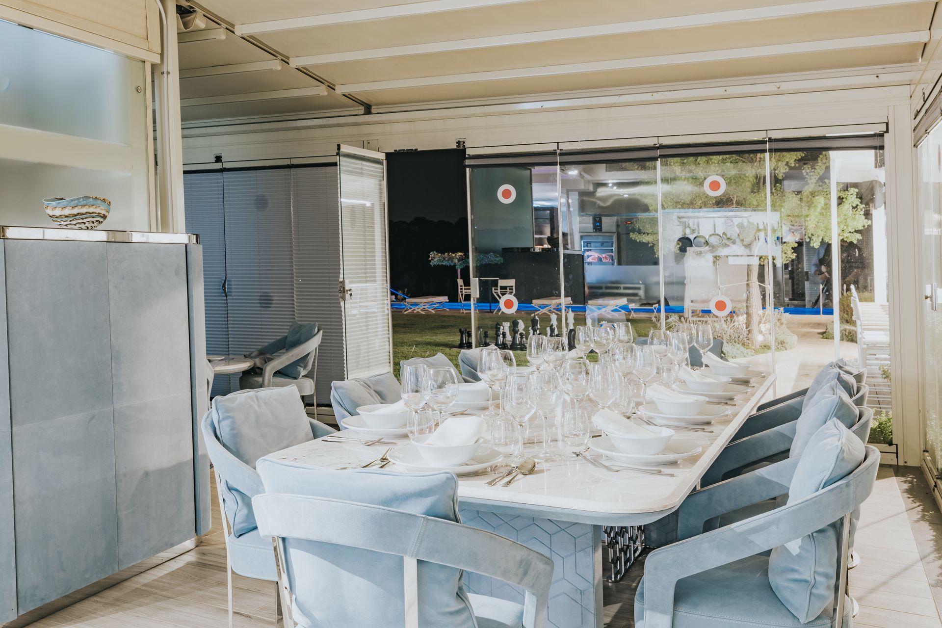 Formal dining table set for guests in a sunlit room. Soft blue chairs and white table setting.