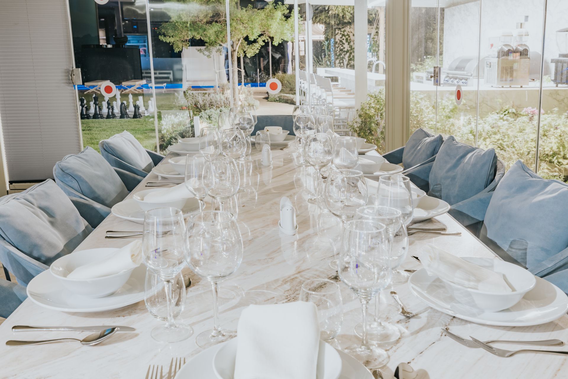 Elegant table setting, white plates, crystal glasses, blue chairs, outdoors background.