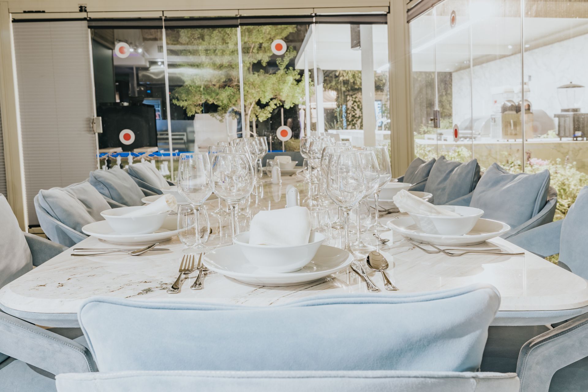 Formal dining table set for a gathering, with blue chairs, white dishes, and clear glassware in a bright room.