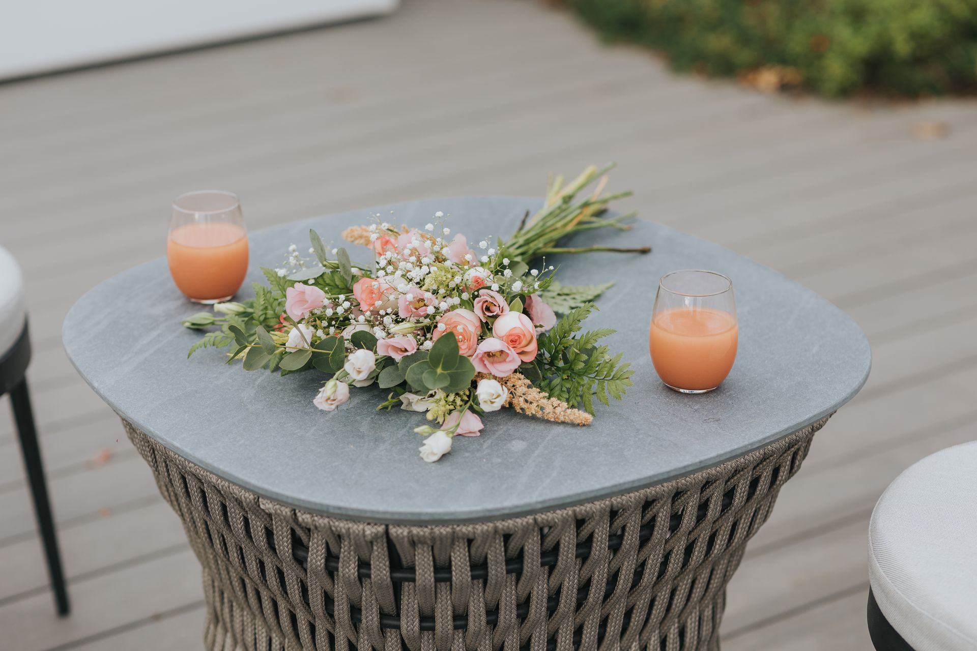 A bouquet of flowers and two drinks sit on a round gray table.
