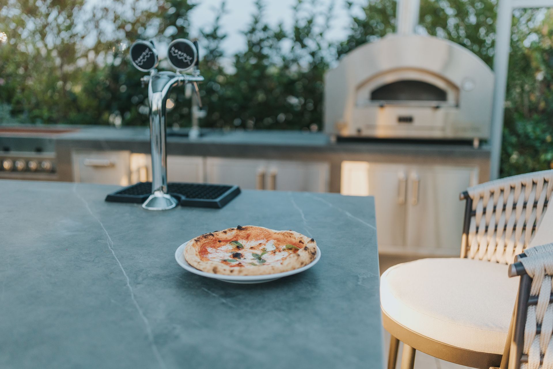 Outdoor kitchen with pizza on a counter, beer tap, and pizza oven.