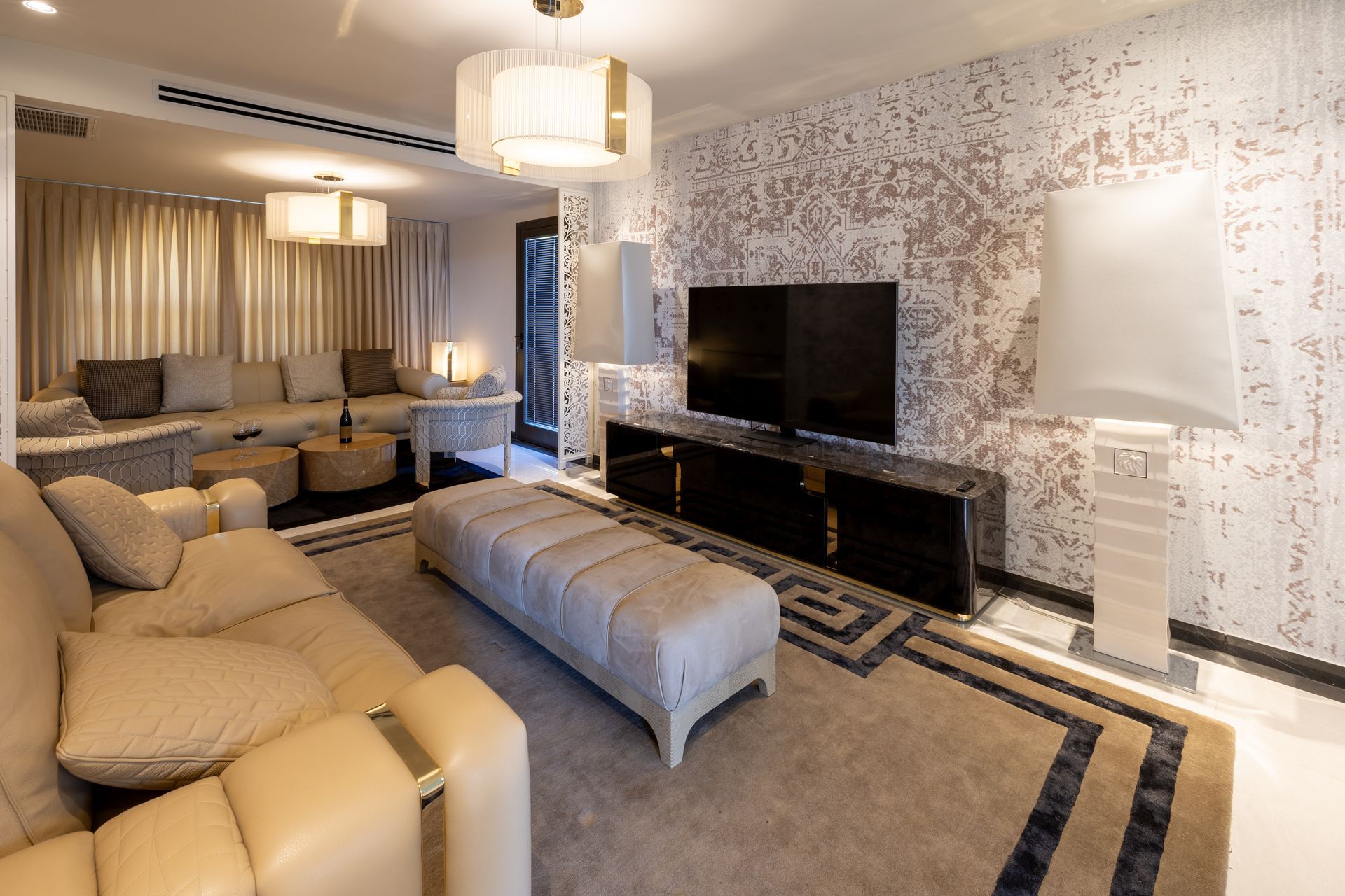 Luxurious living room with beige and gold accents, featuring sofa, TV, and patterned rug.