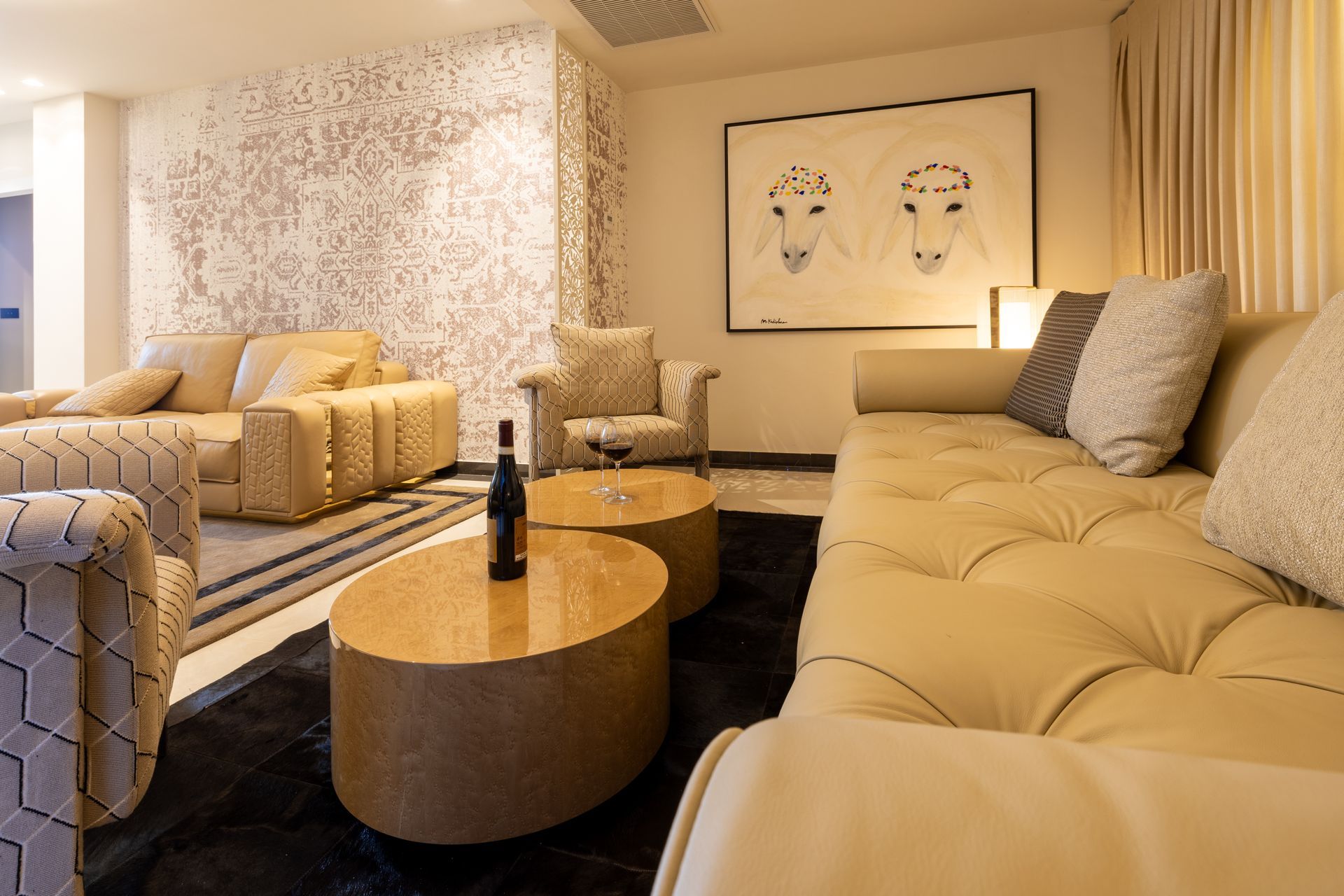 Upscale living room with beige sofas, armchairs, two round coffee tables, artwork, and a patterned wall.
