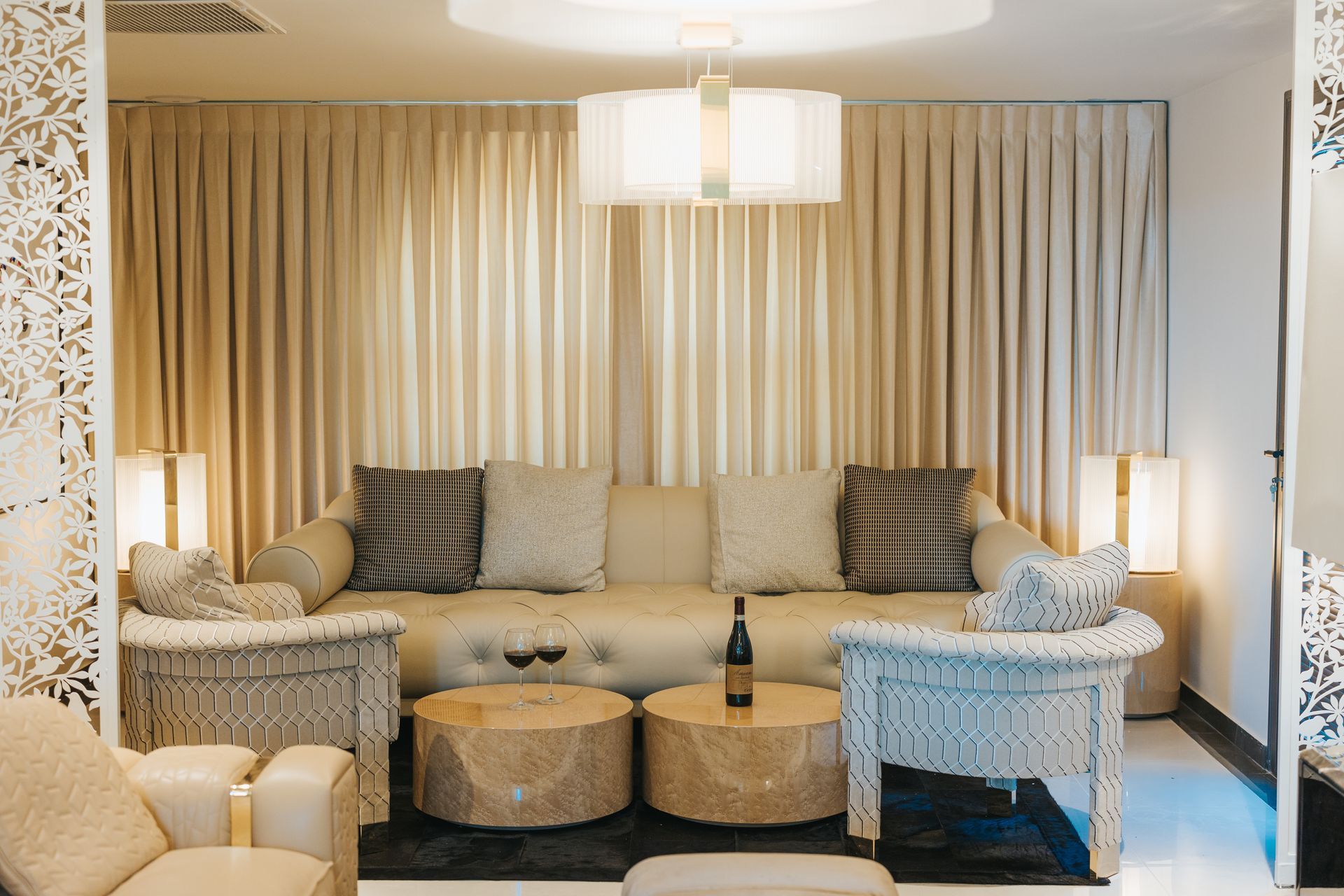 Elegant beige living room with a sofa, two chairs, coffee tables, and a bottle of wine.
