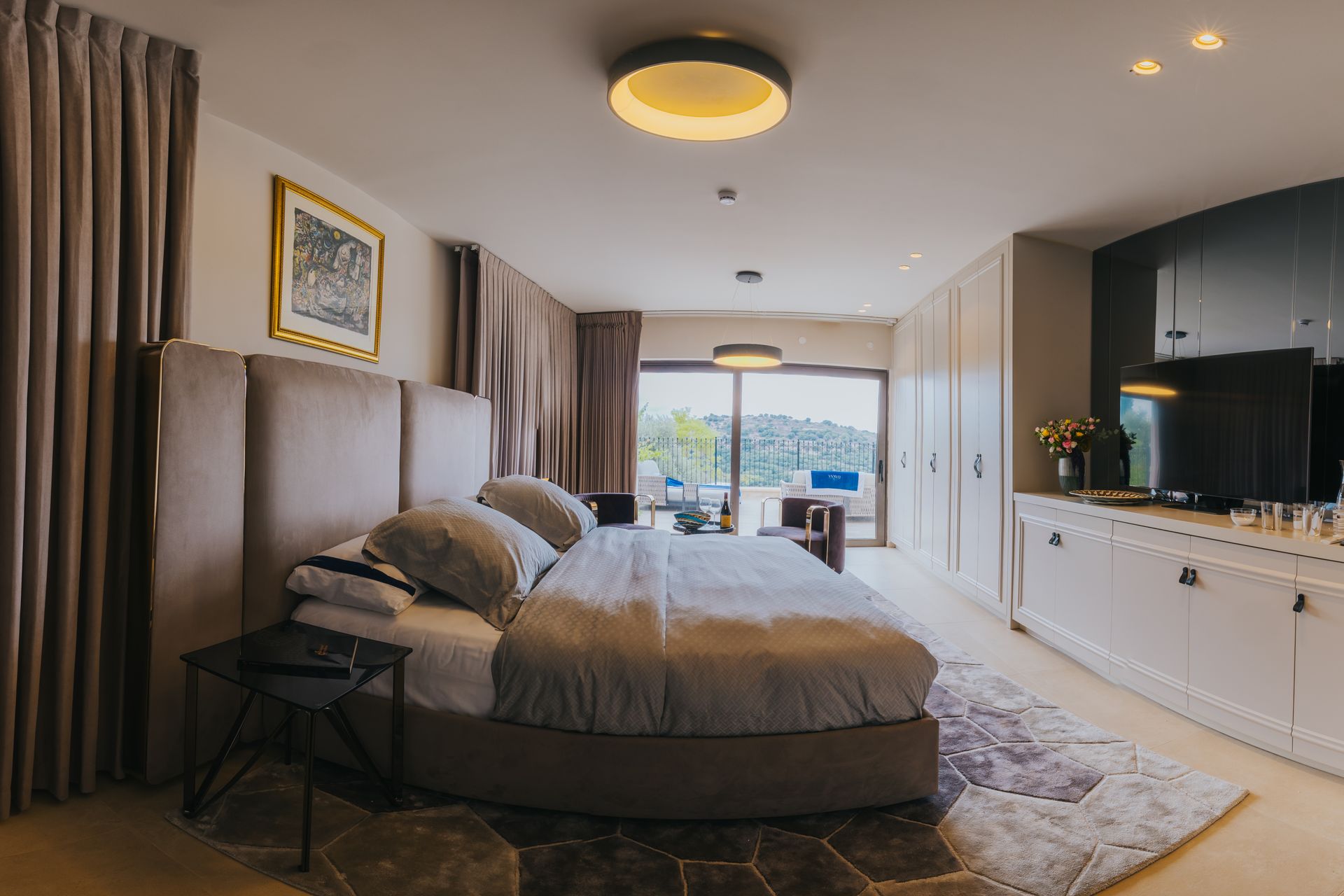 Elegant bedroom with a large bed, neutral tones, sliding doors to a view, and built-in storage.