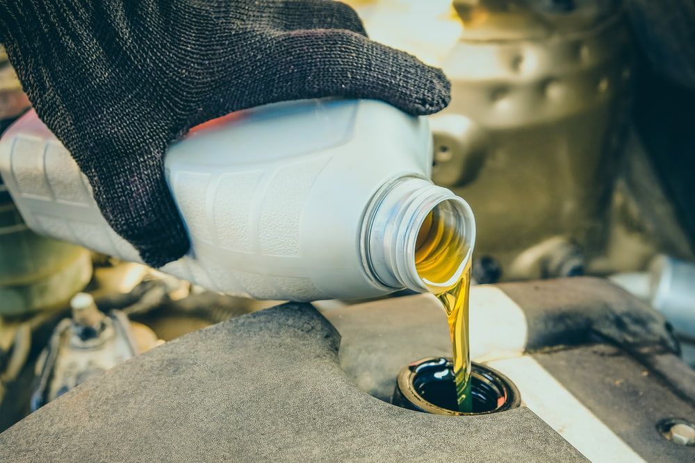Gloved Hand Pouring Oil From a White Jug Into a Car Engine — Burcher EFI & Service Centre in Orange, NSW