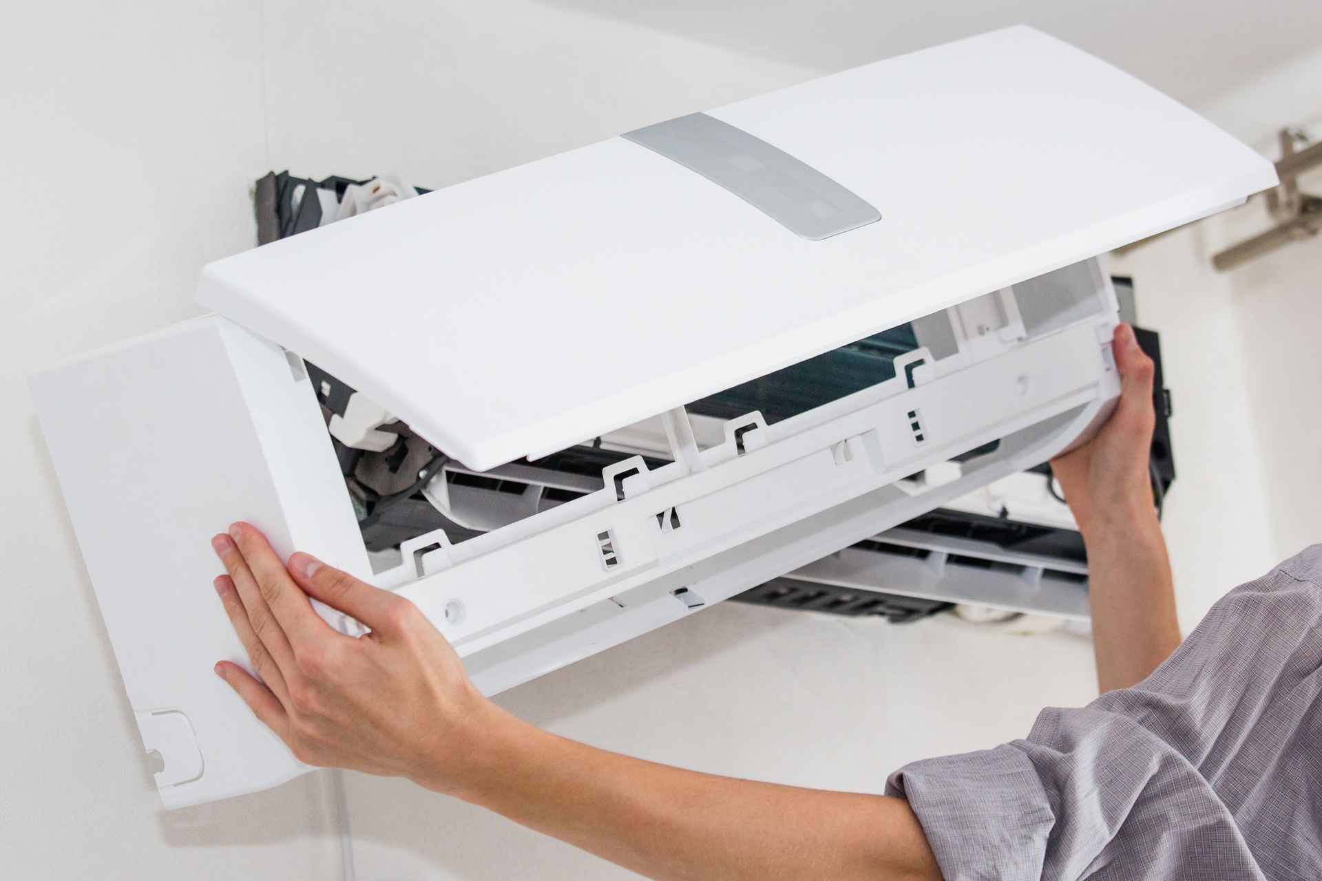 Person removing a white wall-mounted air conditioner cover for maintenance Person removing a white wall-mounted air conditioner cover for maintenance