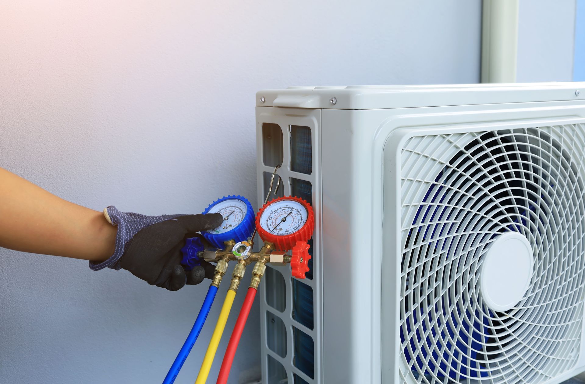 Gloved hand attaching manifold gauges to an outdoor air conditioner unit Gloved hand attaching manifold gauges to an outdoor air conditioner unit