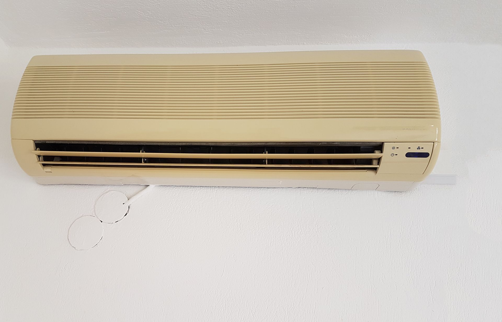 Wall-mounted beige air conditioner on a white wall with a hanging pull chain