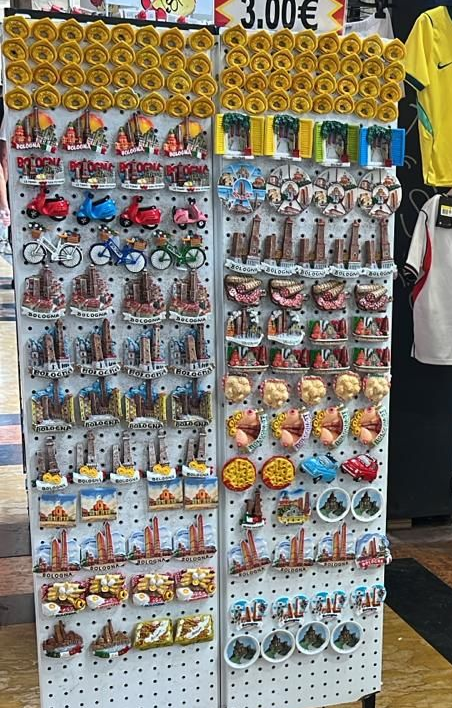Espositore per souvenir turistici con calamite colorate, portachiavi e cianfrusaglie su un cavalletto stradale.
