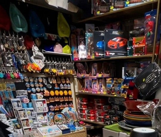 Scaffali disordinati di negozi di giocattoli e articoli da regalo, pieni zeppi di oggetti colorati e modellini di auto.