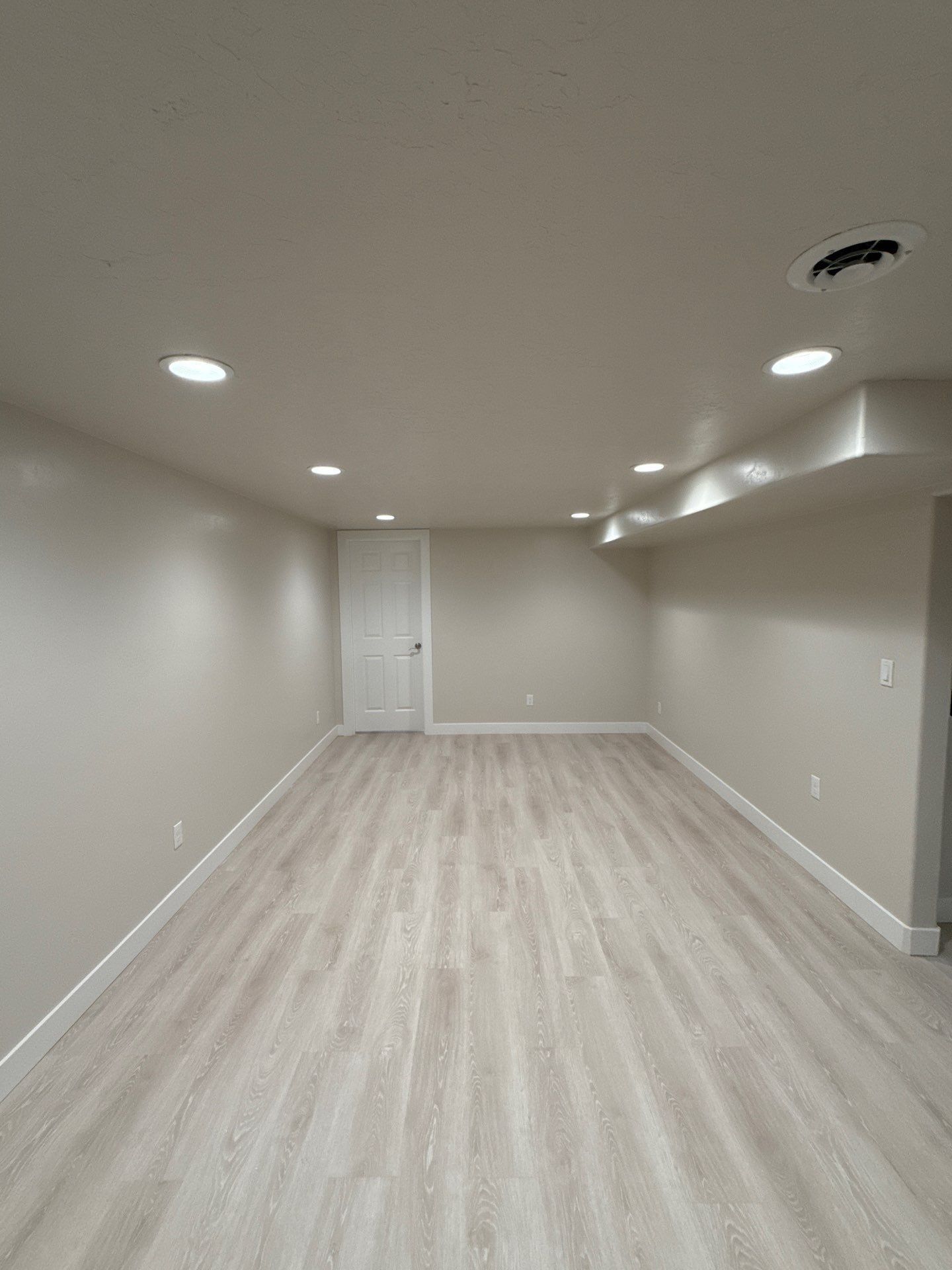 Empty Beige Room with Light Wood Floors, Recessed Ceiling Lights, and A White Door at The Far End in Twin Falls, ID
