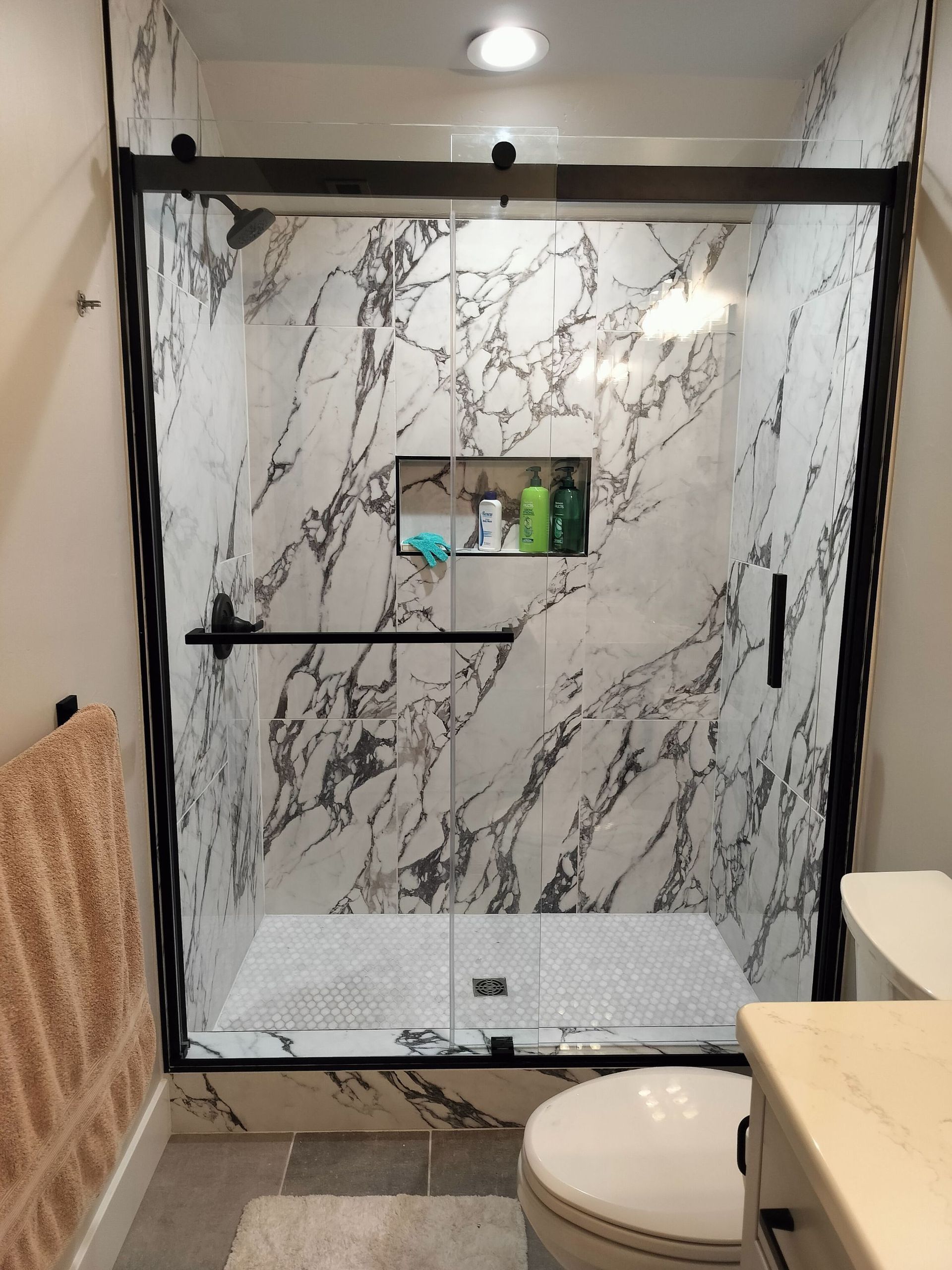 Marble-Tile Shower with Black Frame, Small Bench, and Round Toilet in A Compact Bathroom in Twin Falls, ID