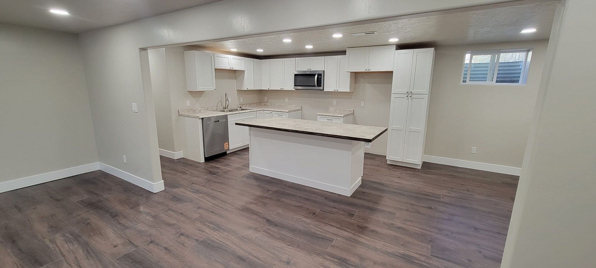 Empty Modern Kitchen and Dining Area with White Cabinets, Island, and Dark Wood Flooring in Twin Falls, ID