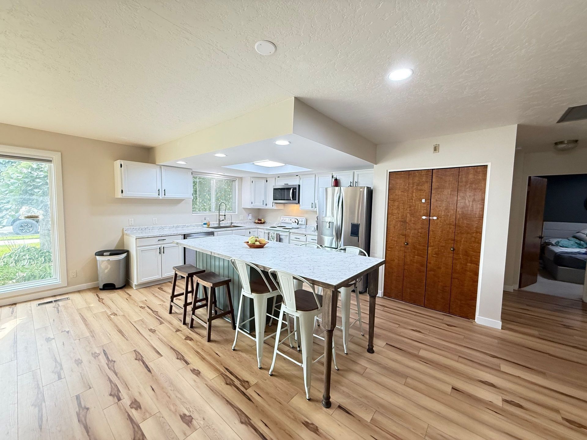 Bright Kitchen and Dining Area with Island, Stools, White Cabinets, Wood Floors, and Double Closet Doors in Twin Falls, ID