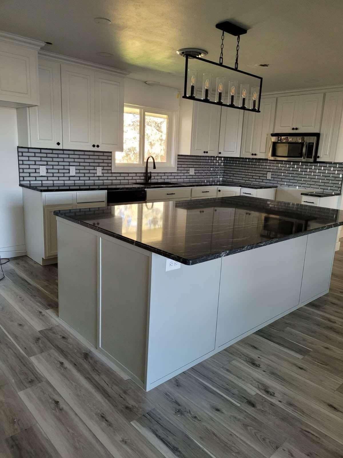 Modern Kitchen with White Cabinets, Black Island Countertop, Gray Tile Backsplash, and Wood-Look Floors in Twin Falls, ID