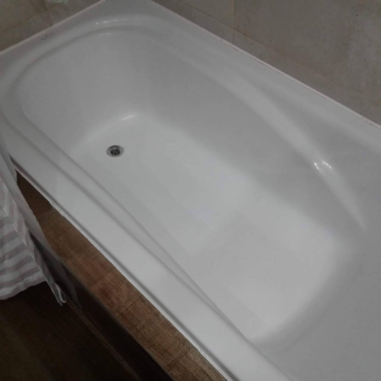 Lavabo y bañera de esquina blancos con grifo cromado y dispensador de jabón.