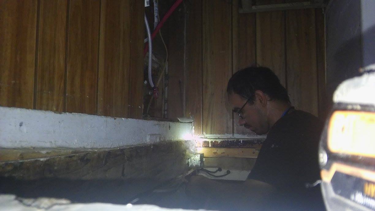 A man is looking under a wooden wall with a flashlight.