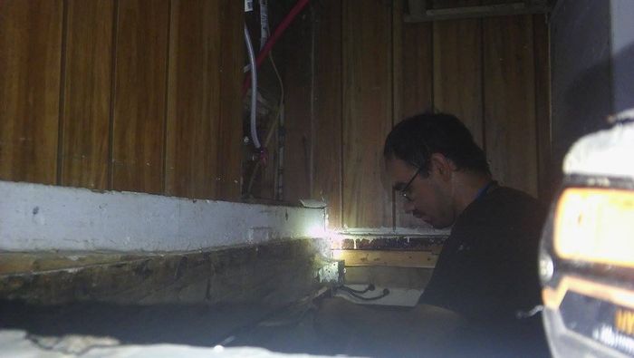 A man is looking under a wooden wall with a flashlight.