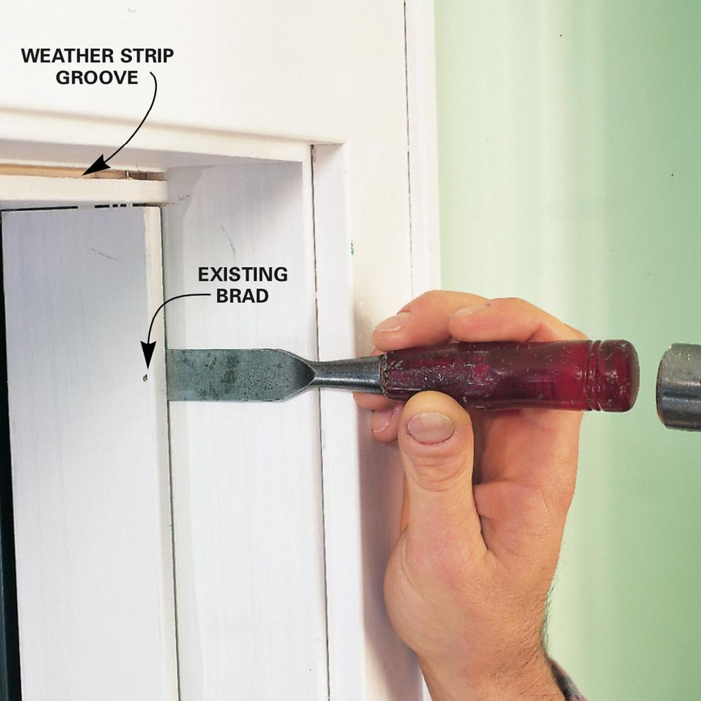 A person is using a chisel to remove a weather strip from a window frame