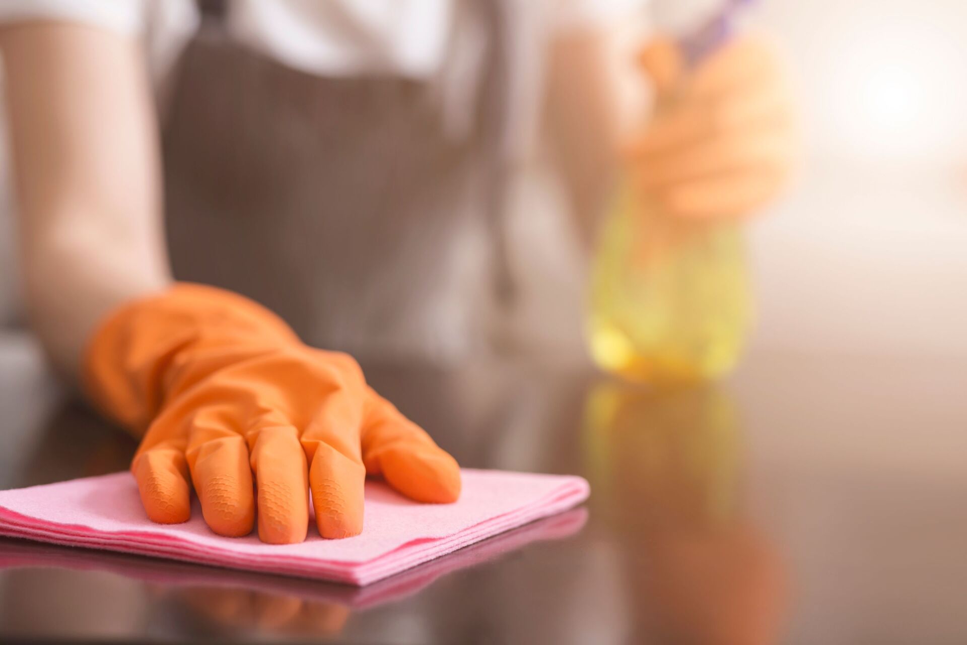 A person wearing orange gloves is cleaning a table with a cloth.