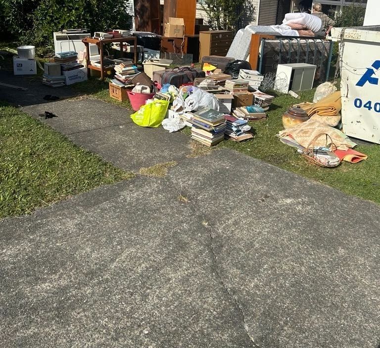 Outdoor curbside pile of assorted household junk, boxes, and bags on a driveway beside a road.