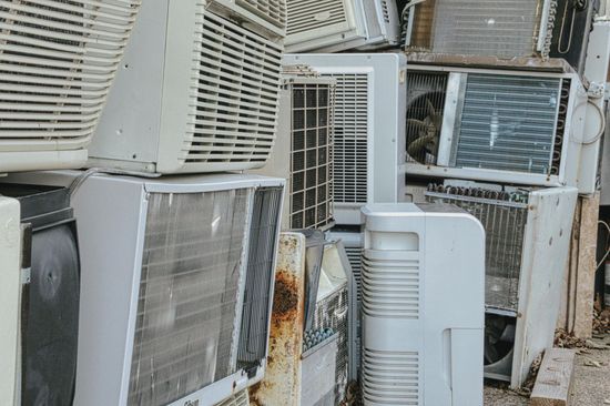 Stacked old air conditioners and metal units in a pile of scrap, with rust and grime visible.