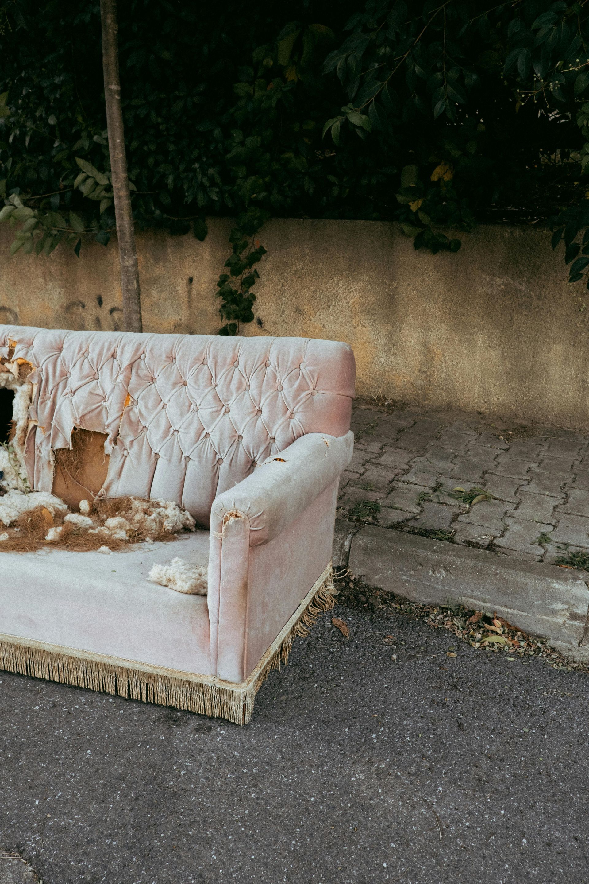 Damaged pink sofa on a roadside beside a stone wall and greenery
