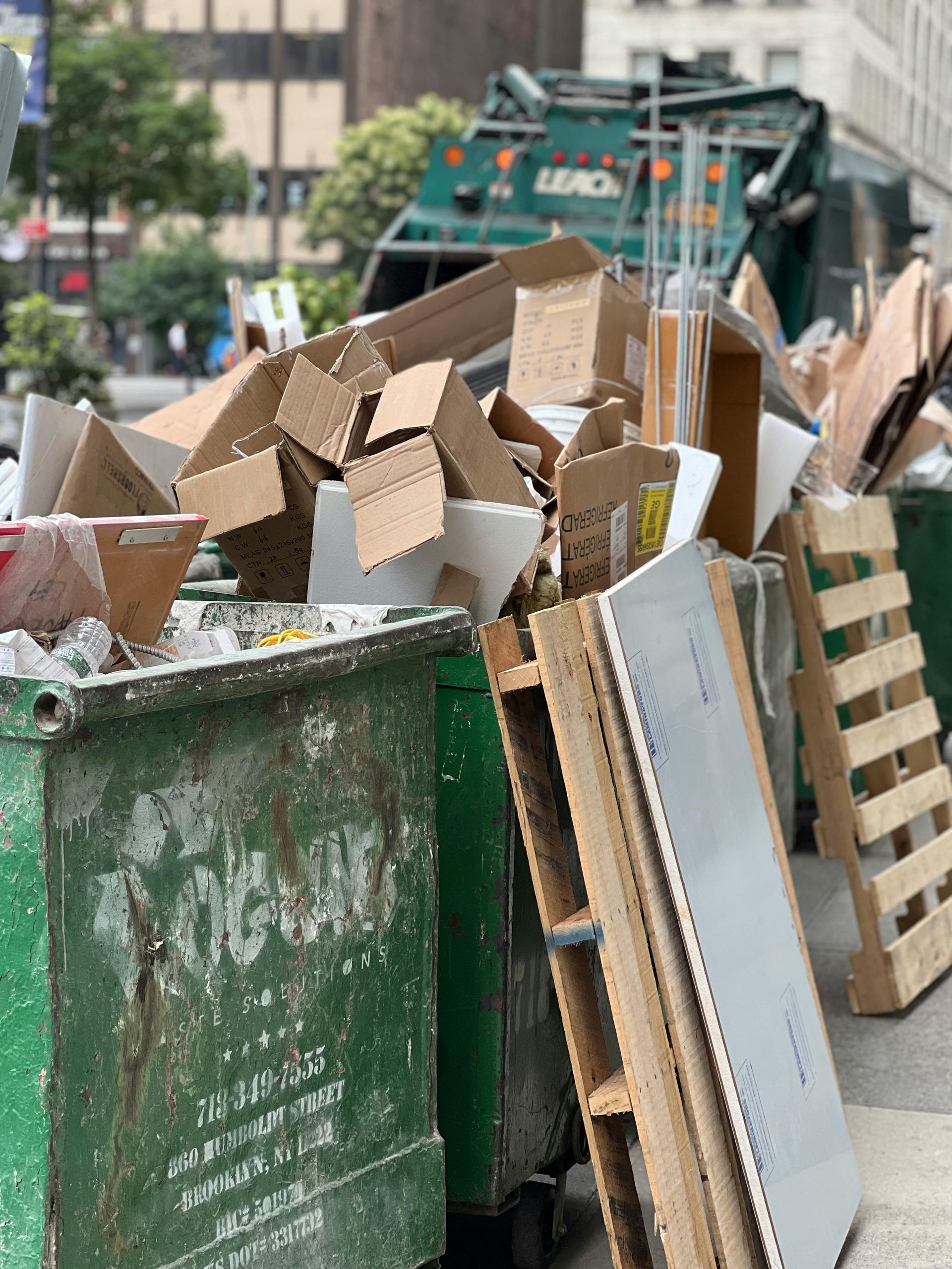 Overflowing green dumpsters filled with cardboard boxes and trash outdoors