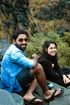 Two people sitting on a rocky ledge outdoors, smiling at the camera.