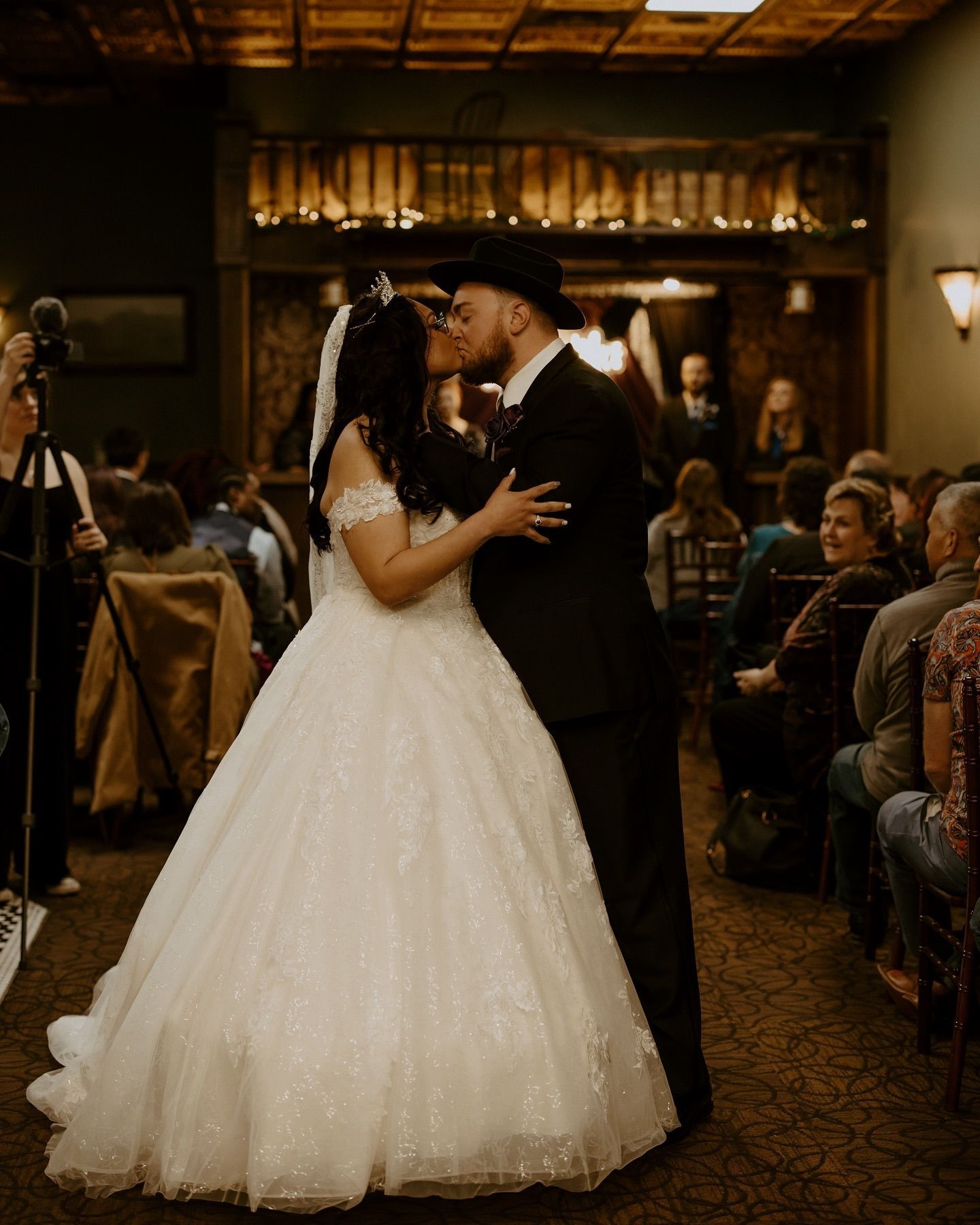 A bride and groom kissing at their wedding ceremony in front of a crowd.