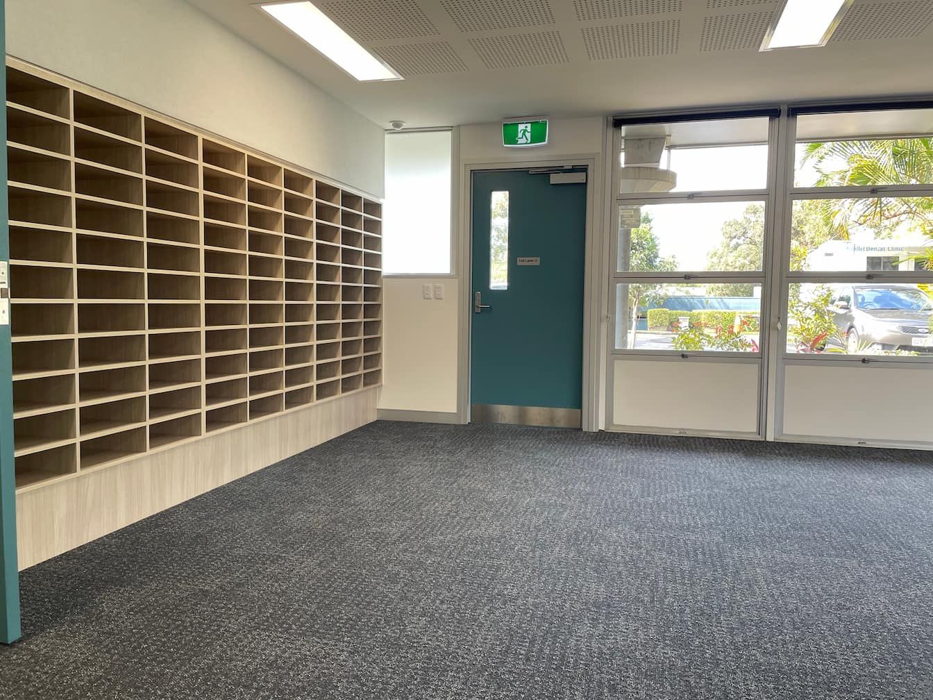 an empty room with a green exit sign above the door and cabinetry on the left