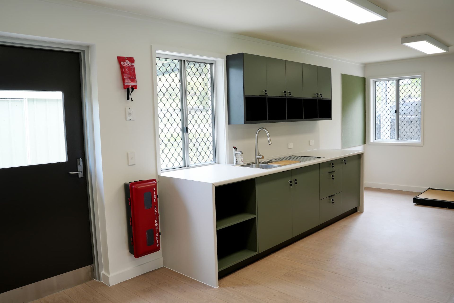a kitchen with green cabinets and a red fire extinguisher on the wall