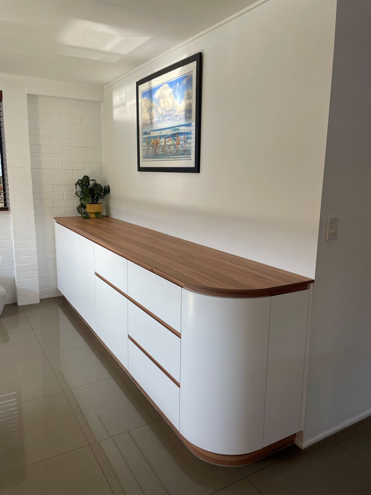 a picture of a beach scene hangs above a long white cabinet