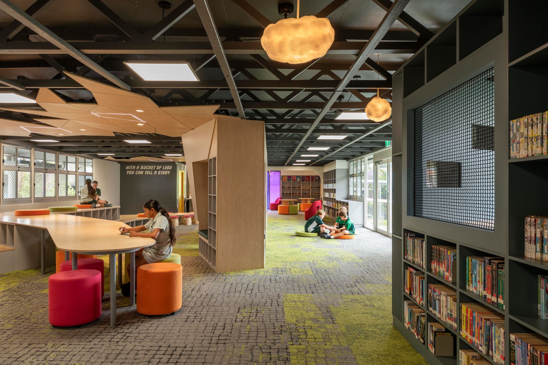 Library interior with bookshelves, reading tables, colorful seating, and children reading.