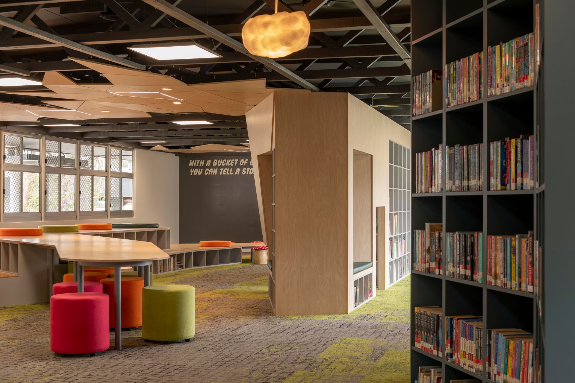 Library interior with bookshelves, seating area with colorful stools, and decorative ceiling.
