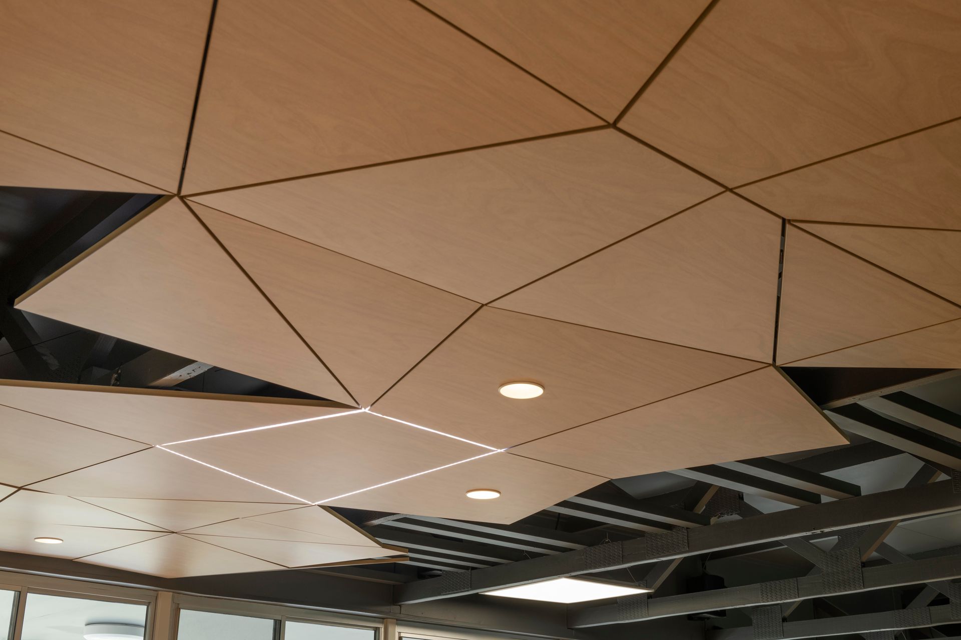 Light wood-paneled ceiling with geometric shapes, recessed lights, and exposed metal structure.