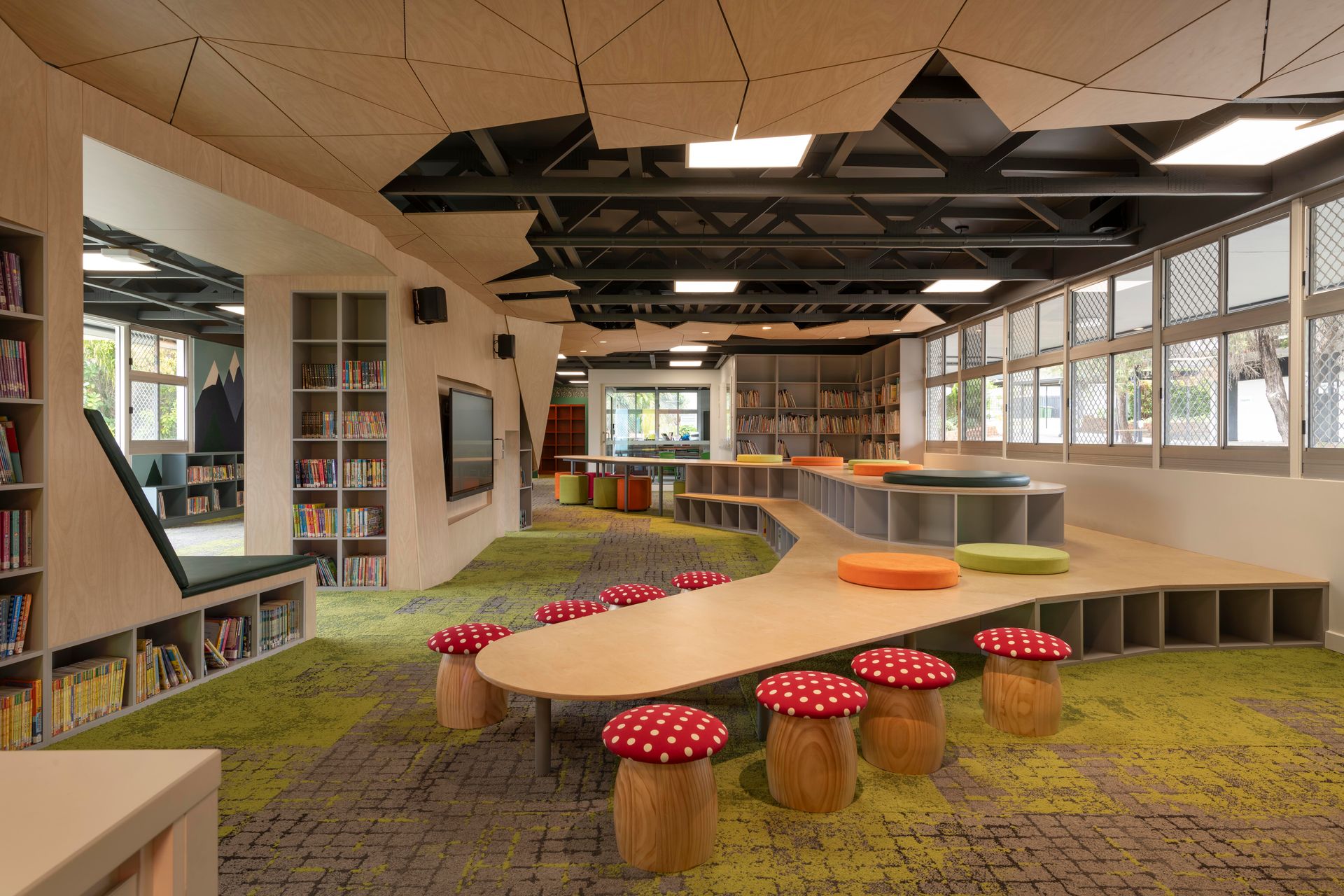 A whimsical library with mushroom stools, long wooden tables, built-in bookshelves, and a green, grassy carpet.