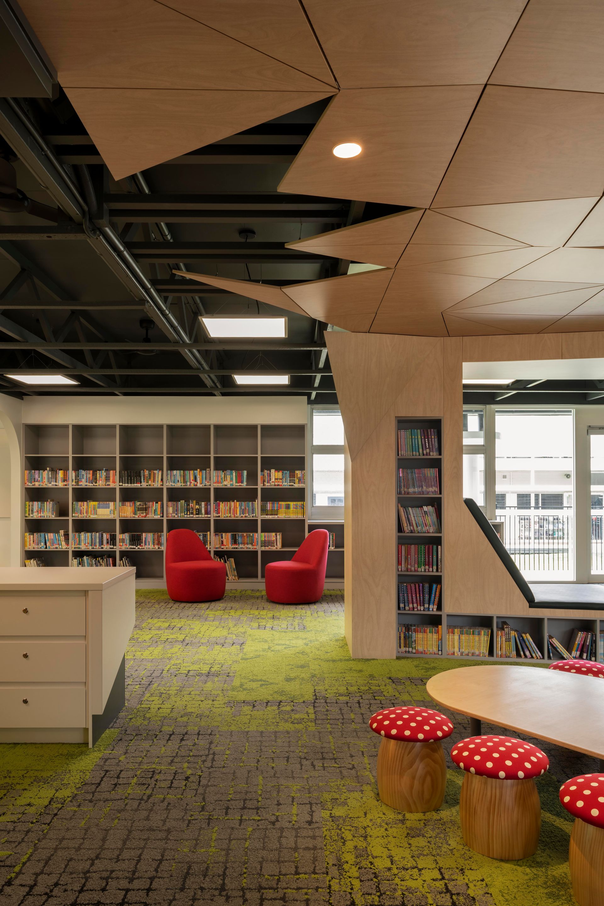 Library interior with bookshelves, red chairs, mushroom stools, and a unique ceiling design.
