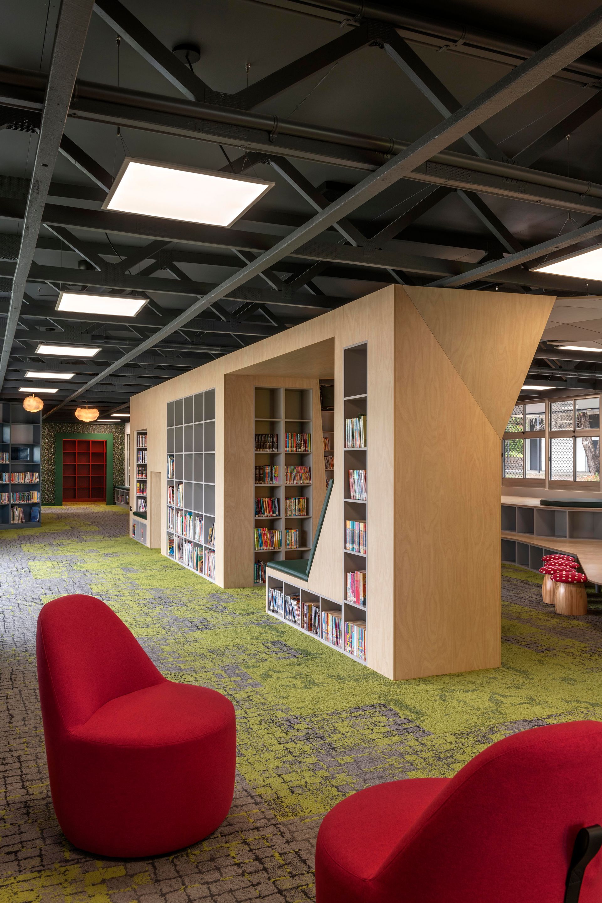 Library interior with red chairs, bookshelves, and green carpet. Black ceiling with lights.
