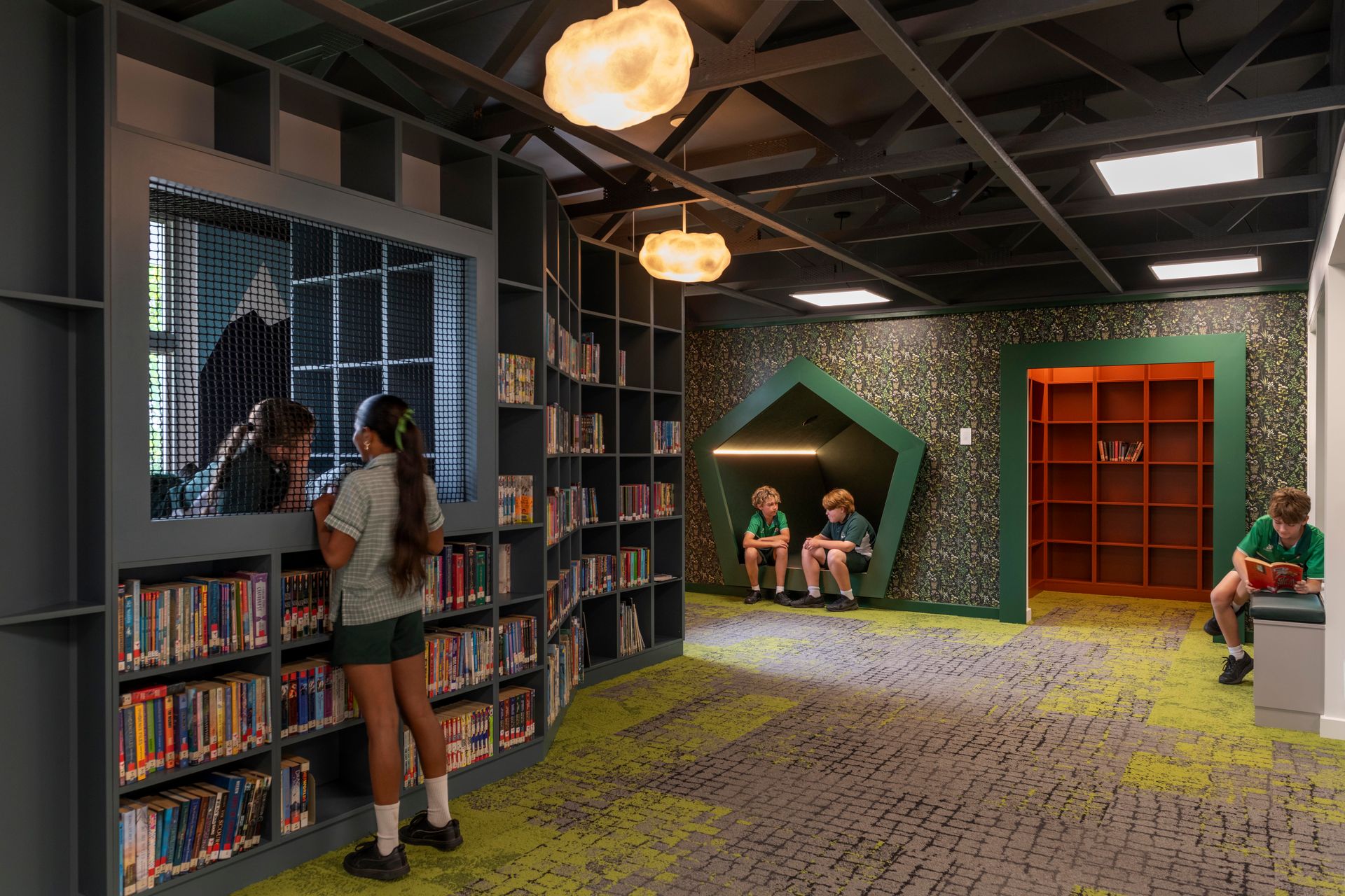 Children's library with bookshelves, reading nook, and students. Green and gray color scheme.