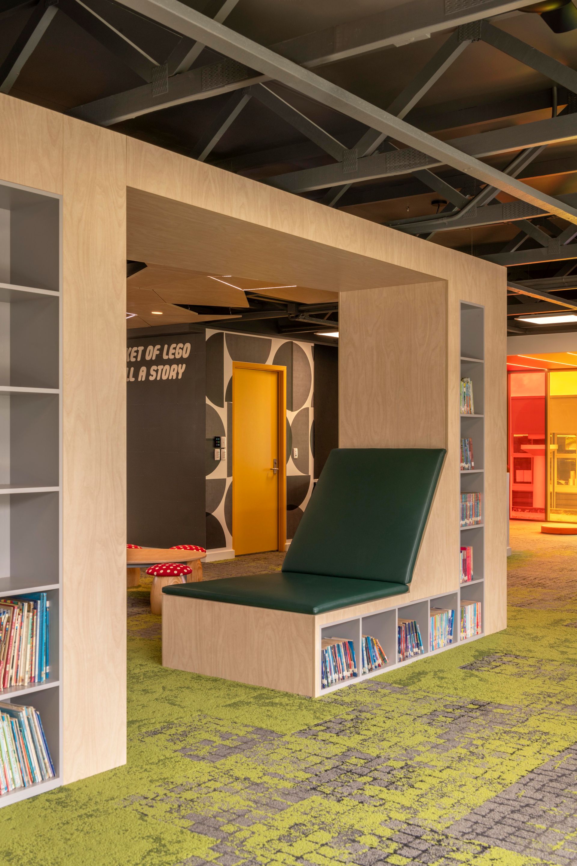 A reading nook with a green seat and built-in bookshelves. The room has light wood paneling and green carpet.