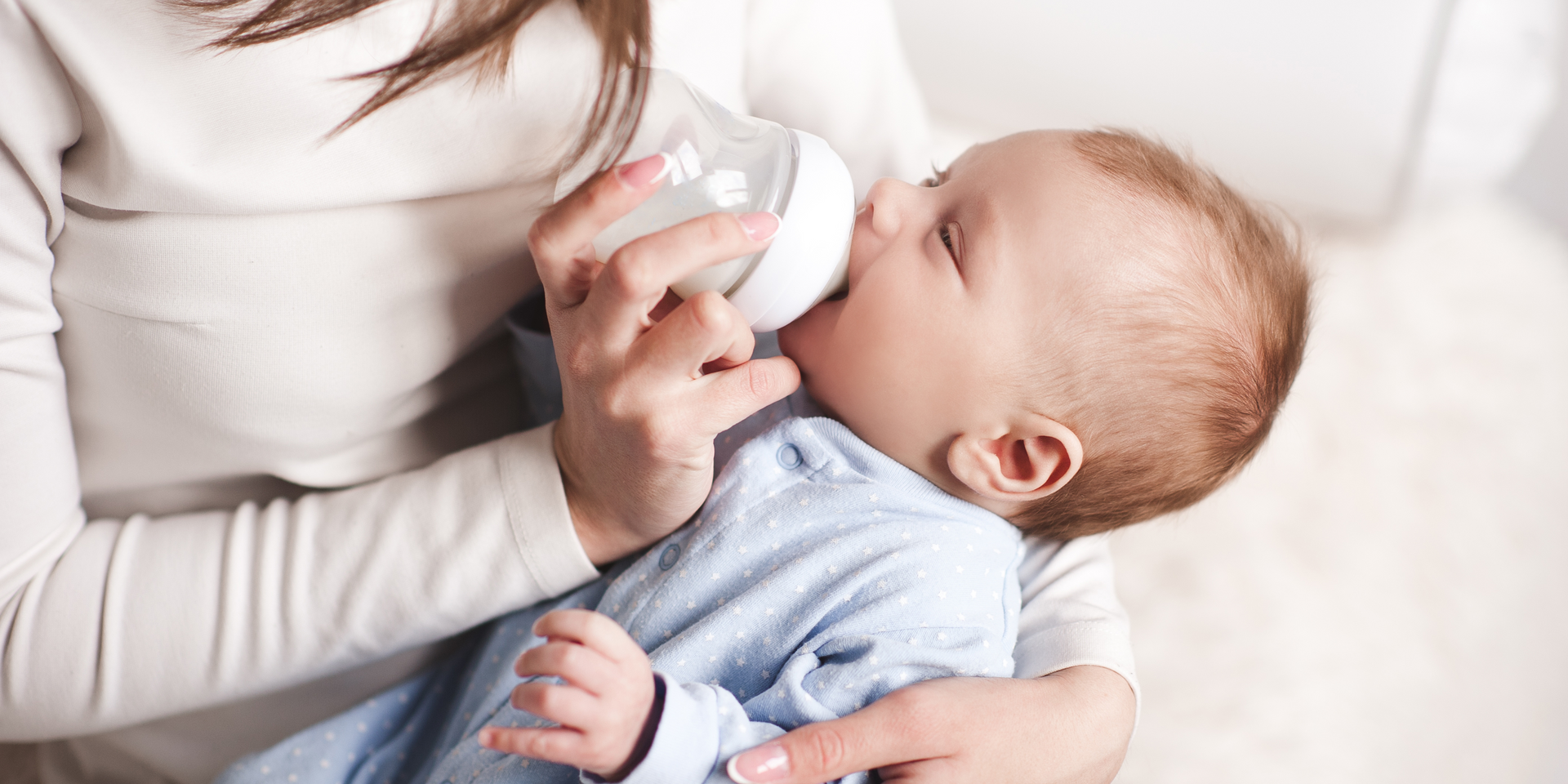 Person feeding a baby with a bottle, close-up indoors