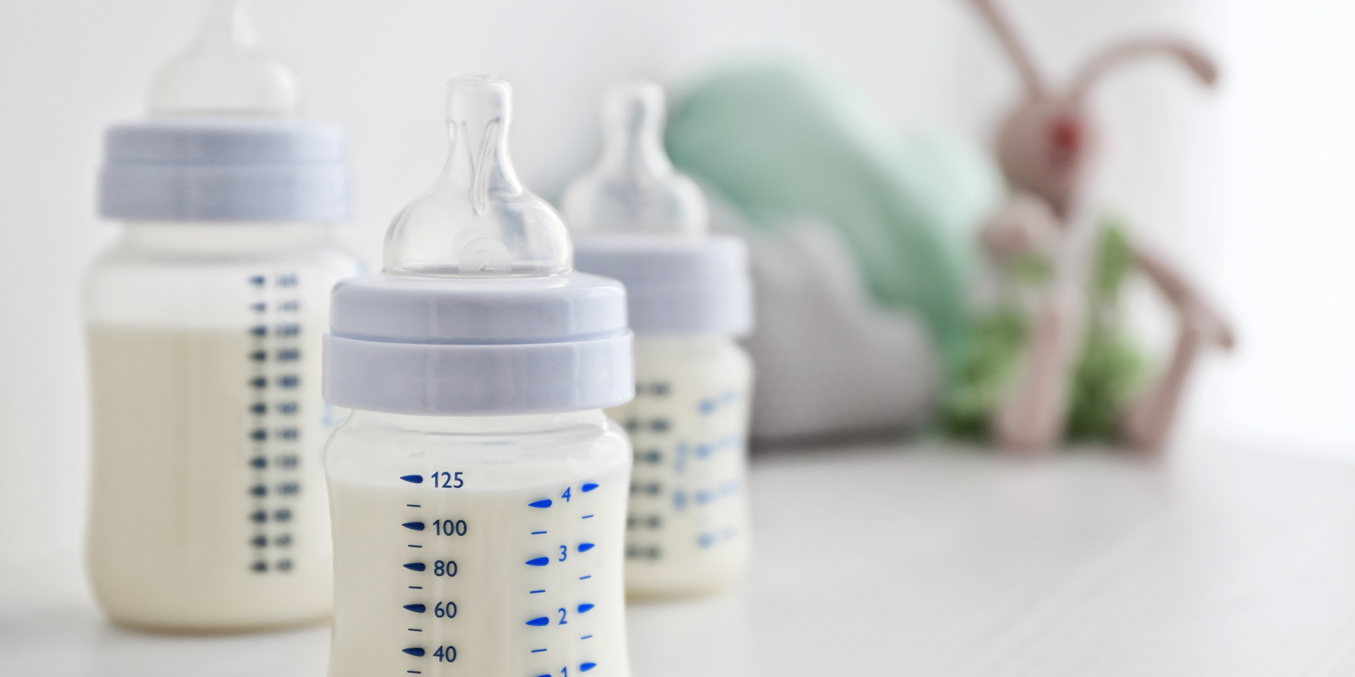 Baby bottles and pacifiers on a white table, with blurred nursery items in the background