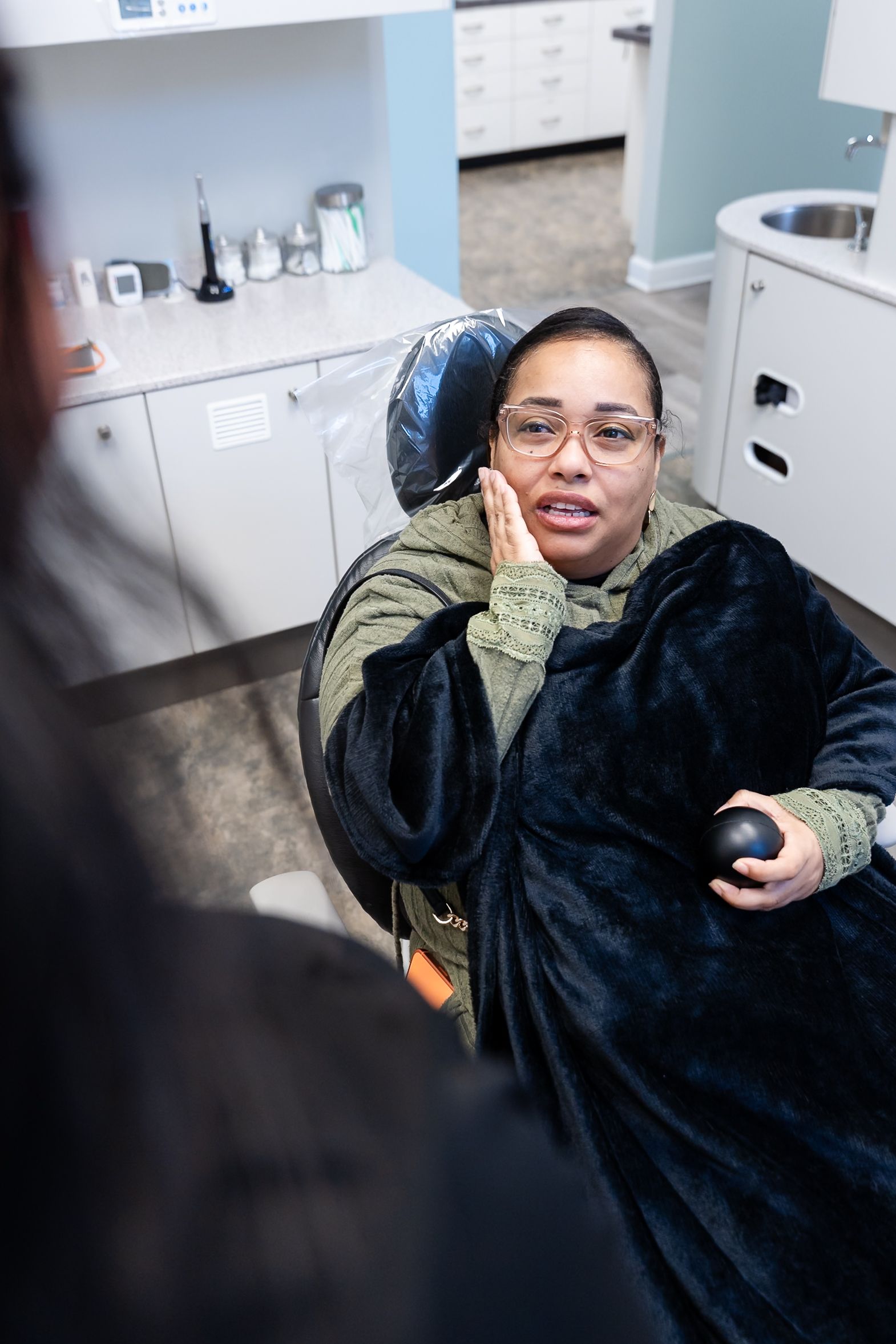 Woman seated in a dental chair holding her cheek at DentCare Now, emergency dentist serving Fairfax, VA