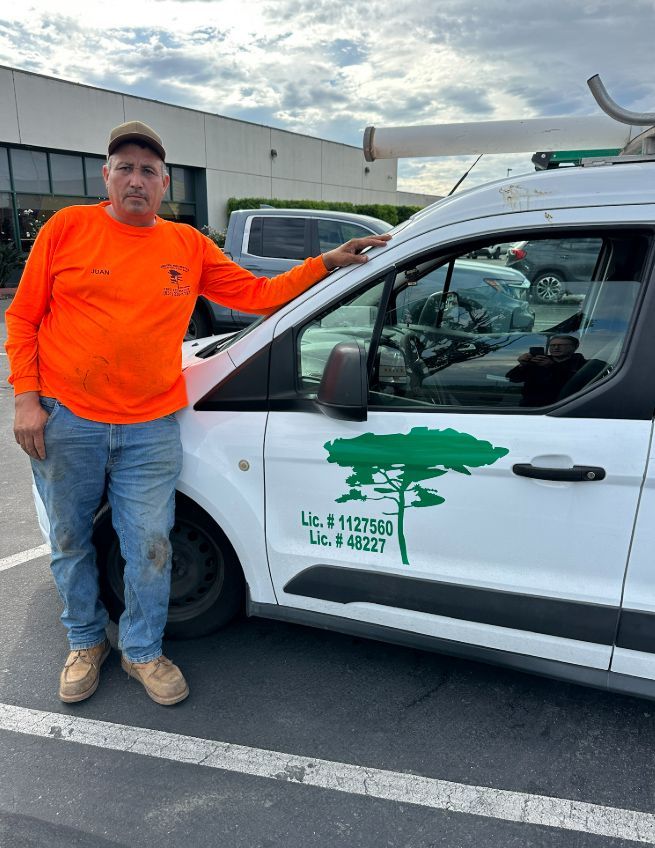Man in orange shirt and jeans beside white van with tree logo.