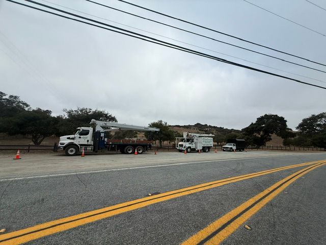 Two utility trucks parked on a roadside near cones under a cloudy sky
