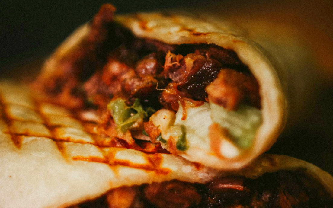 Close-up of a grilled burrito with visible meat, beans, and vegetables inside.